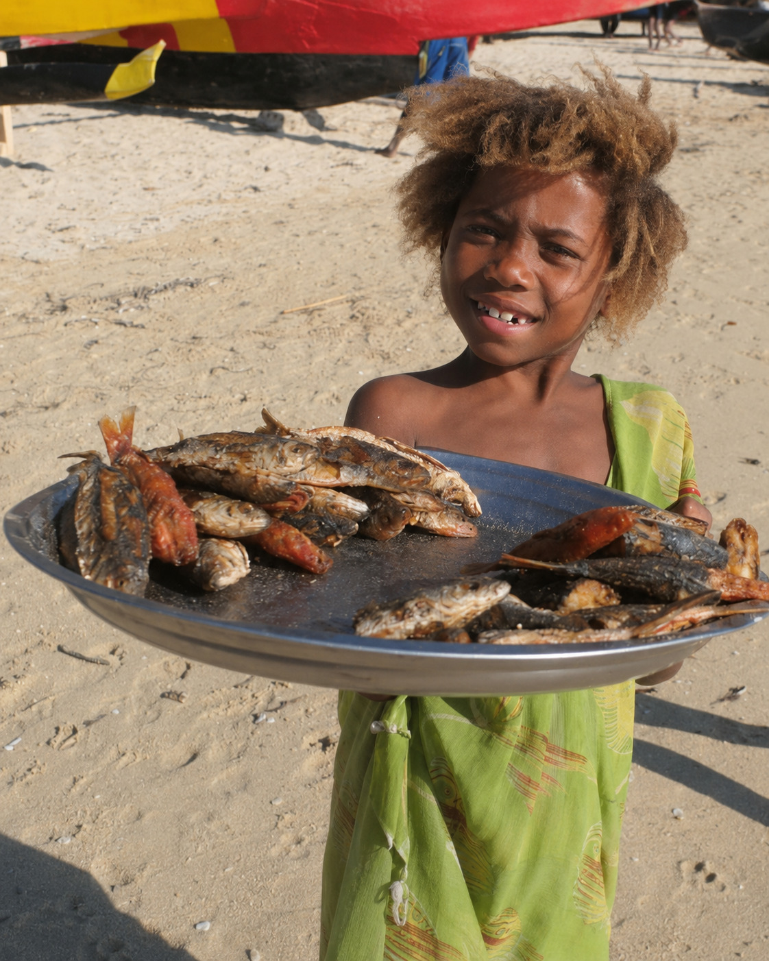Jeune fille présentant des poissons sur une plage malgache
